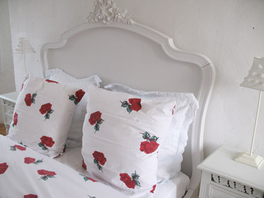 Close up shot of the bed showing the intricate carving on the white bed head. The bed linen is white with lovely photo realistic red roses.